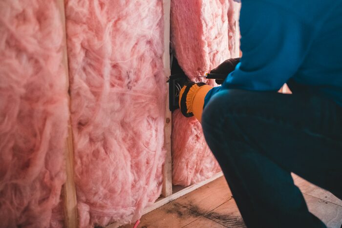 Handwerker verlegt ein Kabel in einer mit rosa Mineralwolle gedämmten Ständerwand – Symbolbild für Dämmung und Wärmepumpen-Förderung 2026