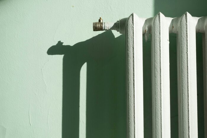 Alter weißer Gussheizkörper an einer mintgrünen Altbauwand im Sonnenlicht – Symbolbild zur Wärmepumpen-Pflicht 2026 und zum GModG