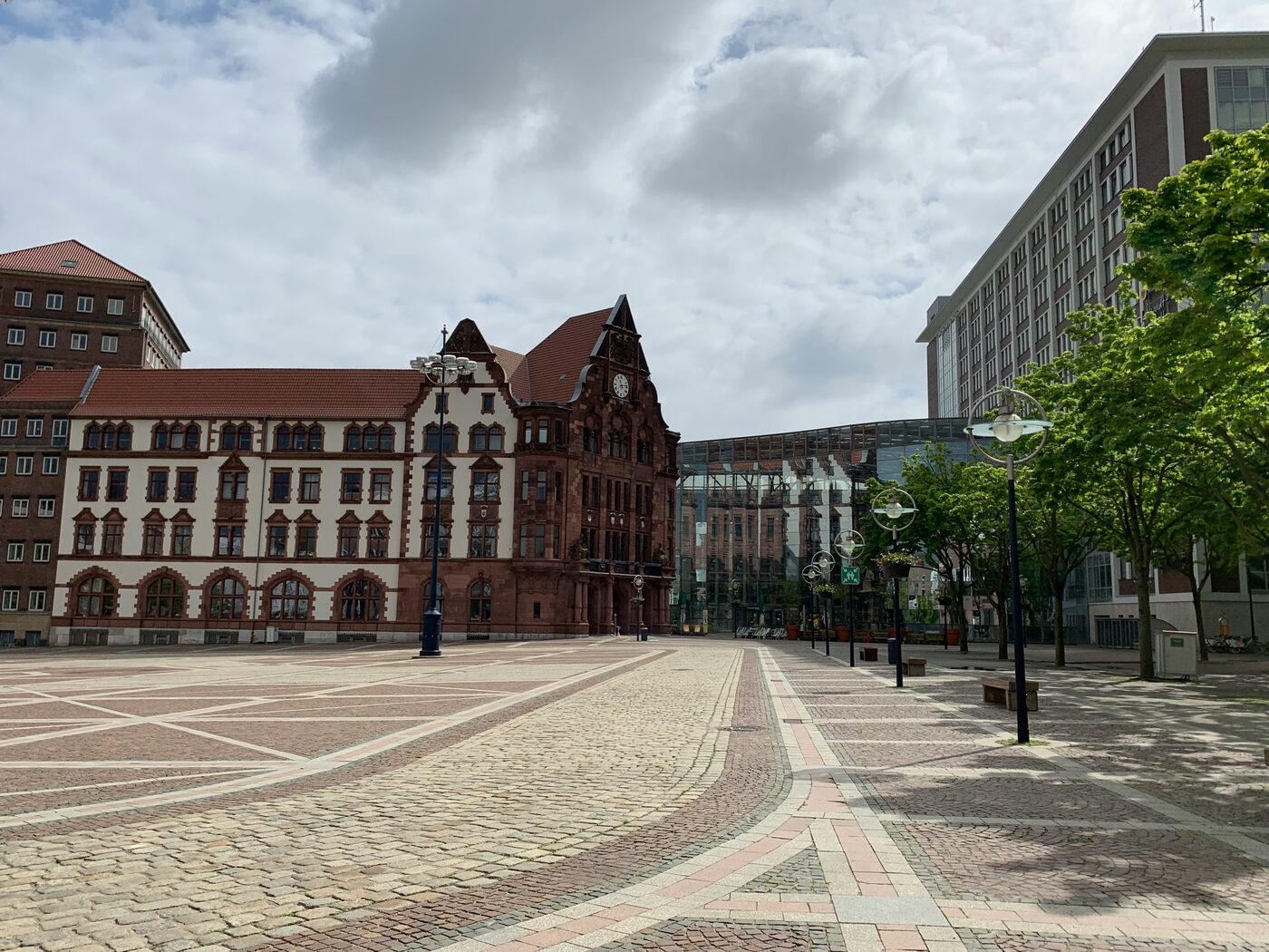 Historisches Altes Stadthaus am gepflasterten Dortmunder Friedensplatz mit modernen Gebäuden und Bäumen unter bewölktem Himmel