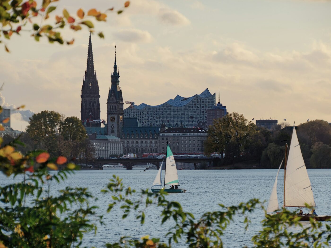Blick über die Hamburger Binnenalster mit Segelbooten, dem Rathausturm und der Elbphilharmonie im Herbst